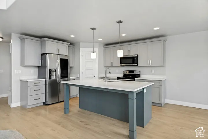 Kitchen featuring gray cabinetry, stainless steel appliances, a center island with a white countertop, and wood-finish flooring