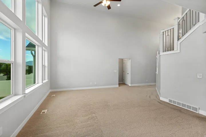Vaulted ceilings with a ceiling fan, wall of large windows, neutral carpeting, and a staircase with a decorative railing