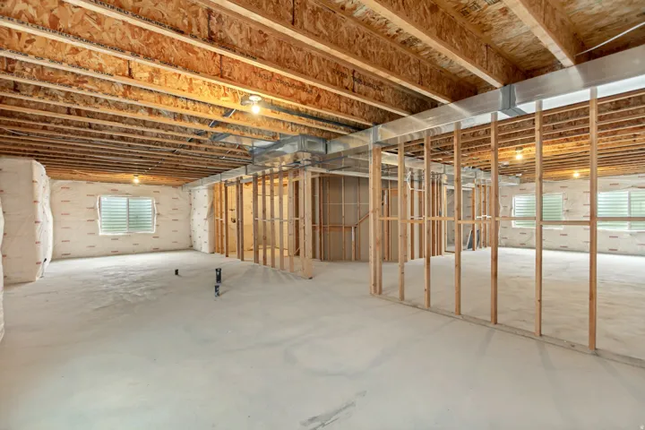 Unfinished basement featuring exposed wood joists, concrete flooring, perimeter insulation, multiple windows, and partial framing
