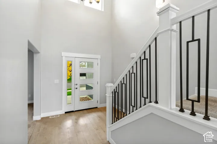 Two-story entryway with wood-finish flooring, a modern front door with frosted glass panels, and a staircase featuring black metal balusters with a white handrail