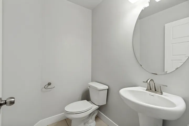 Pedestal sink with brushed nickel faucet, circular mirror, and wall-mounted light fixture