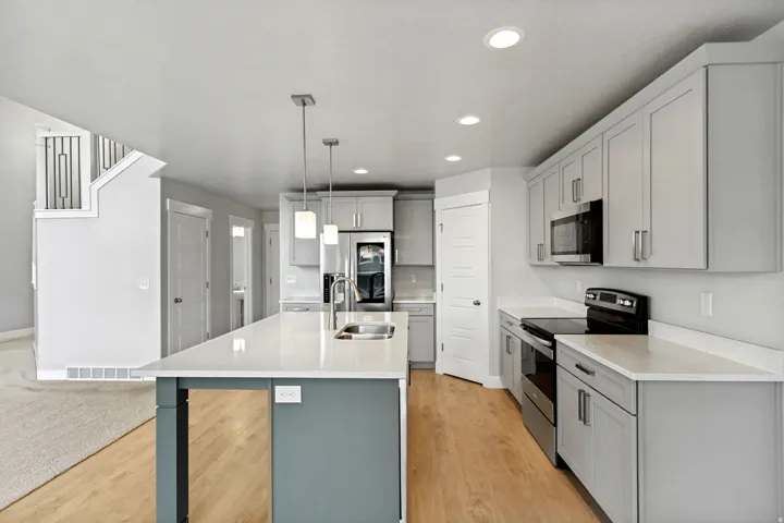 Kitchen featuring an island with pendant lighting, light-toned cabinetry, light countertops, wood-finish flooring, and stainless steel appliances