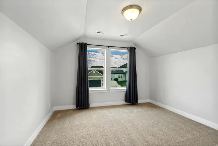 Carpeted room featuring a double window with black curtain rod, sloped ceilings, and a flush-mount light fixture