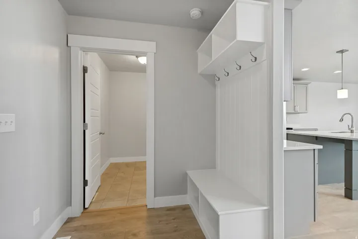 Built-in mudroom bench with upper cubbies and coat hooks, wood-finish flooring, and a contemporary kitchen with pendant lighting