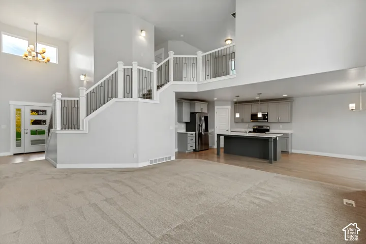 Vaulted ceilings, a grand staircase with decorative railing, and an open-concept kitchen with an island and stainless steel appliances