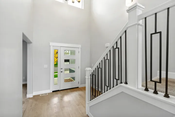 Two-story entryway with wood-finish flooring, a modern front door with frosted glass panels, and a staircase featuring black metal balusters with a white handrail