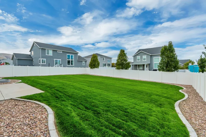 Expansive backyard featuring a manicured lawn, concrete patio, gravel landscaping, and white privacy fencing