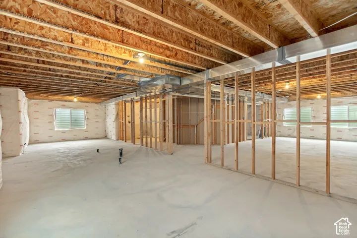 Unfinished basement featuring exposed wood joists, concrete flooring, perimeter insulation, multiple windows, and partial framing