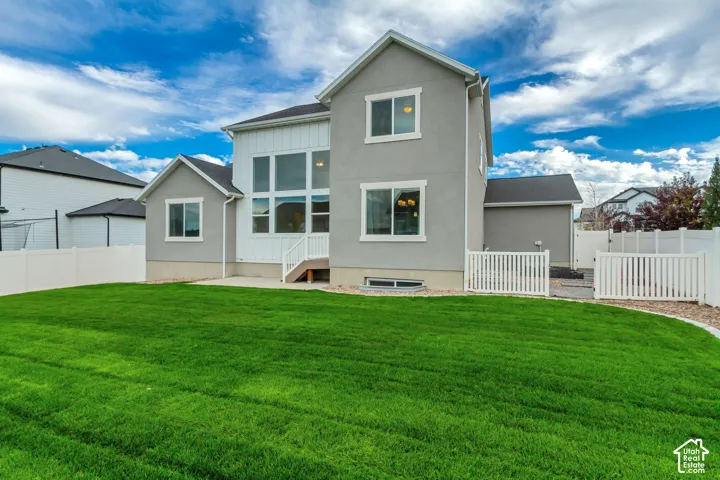 Expansive green lawn with a privacy fence, concrete patio, multi-pane windows, and a stucco and siding exterior