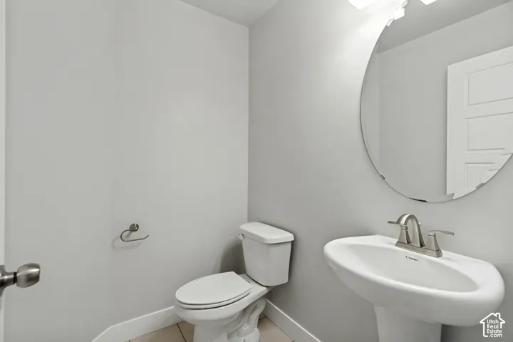 Pedestal sink with brushed nickel faucet, circular mirror, and wall-mounted light fixture