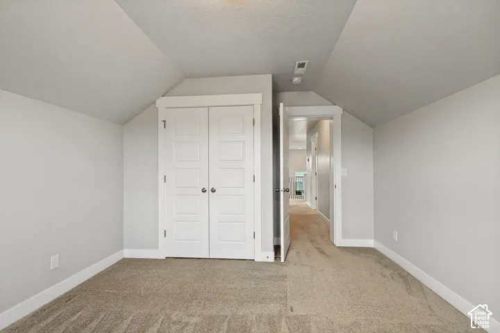 Sloped ceiling with recessed lighting, light-toned carpeting, and a white paneled bi-fold closet door