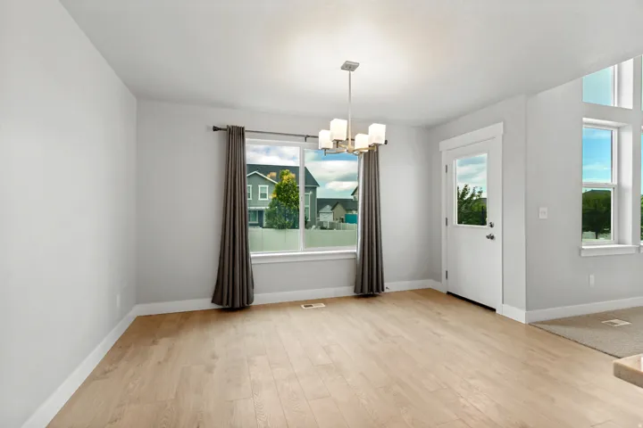 Light wood-finish flooring, a contemporary chandelier, multiple windows, and a white entry door