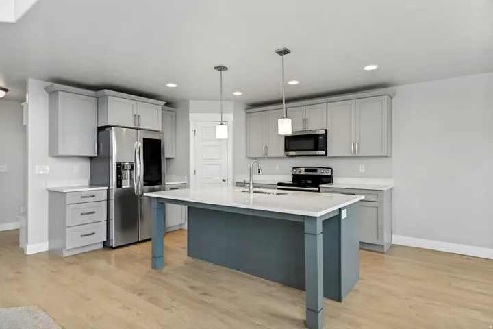 Kitchen featuring gray cabinetry, stainless steel appliances, a center island with a white countertop, and wood-finish flooring
