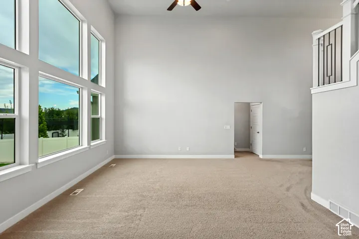 Expansive living space featuring a high ceiling, multiple large windows, light brown carpet flooring, and a decorative staircase railing