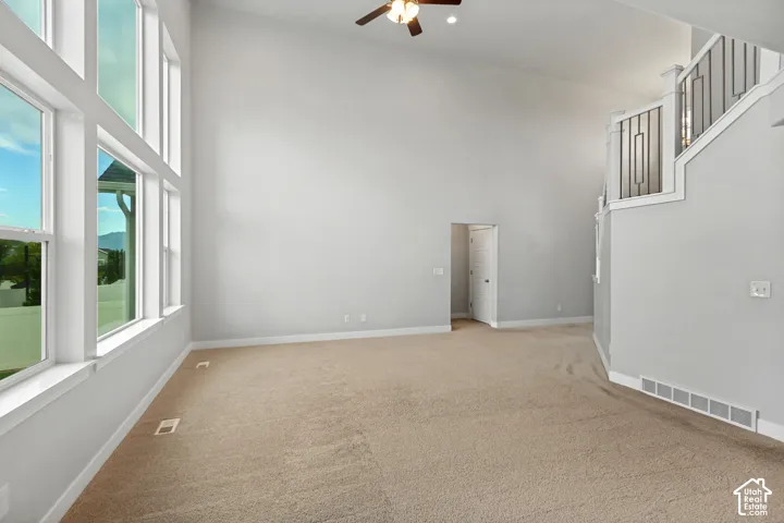Vaulted ceilings with a ceiling fan, wall of large windows, neutral carpeting, and a staircase with a decorative railing