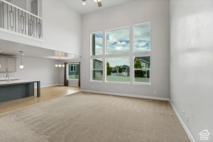 Vaulted ceiling with a ceiling fan, a large window array, and a carpeted floor
