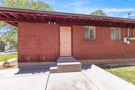 Red brick exterior with an attached metal awning, concrete walkway, and exterior lighting