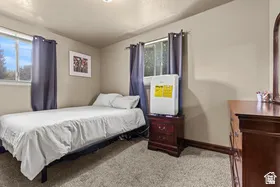 Neutral wall color, recessed ceiling lighting, light-toned carpeting, dual windows with dark drapes, and dark wood trim