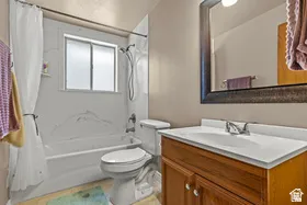 White bathtub and shower combination with a frosted window, wood-finish vanity, and a large framed mirror