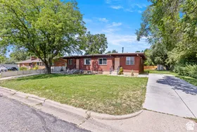 Red brick exterior with a concrete driveway, mature trees, and a grassy front yard
