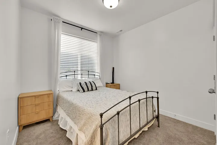 Carpeted flooring, window with blinds and sheer curtains, ceiling-mounted light fixture, white walls, and a door with a metal handle