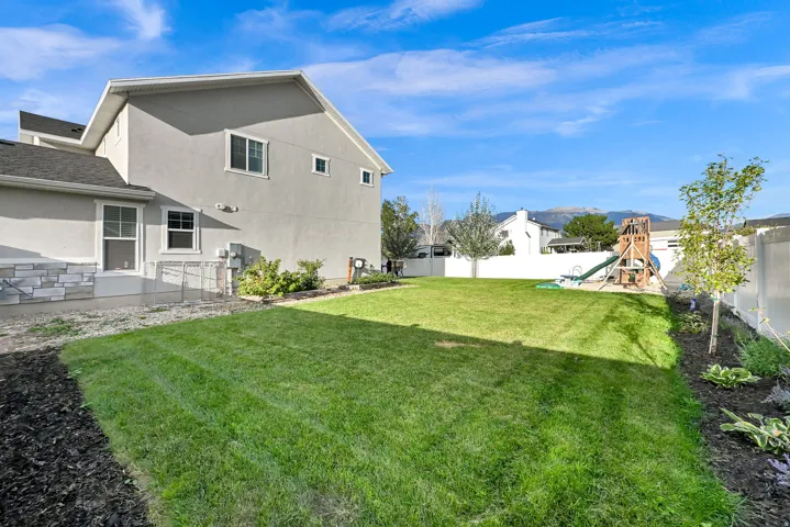 Expansive backyard featuring a manicured lawn, established landscaping, and a mountain backdrop