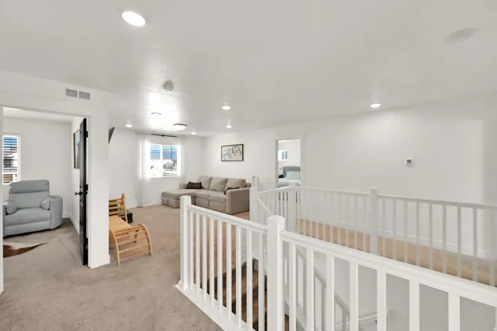 Carpeted landing with white baluster railing, recessed lighting, and multiple windows