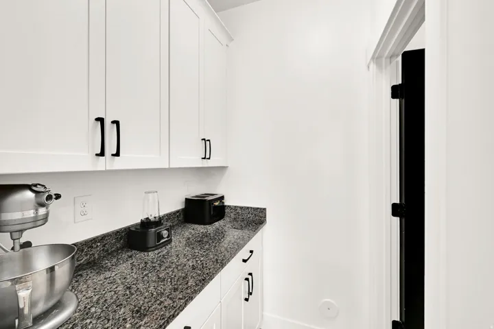White shaker-style cabinetry with matte black hardware, stone-finish countertops, and white trim