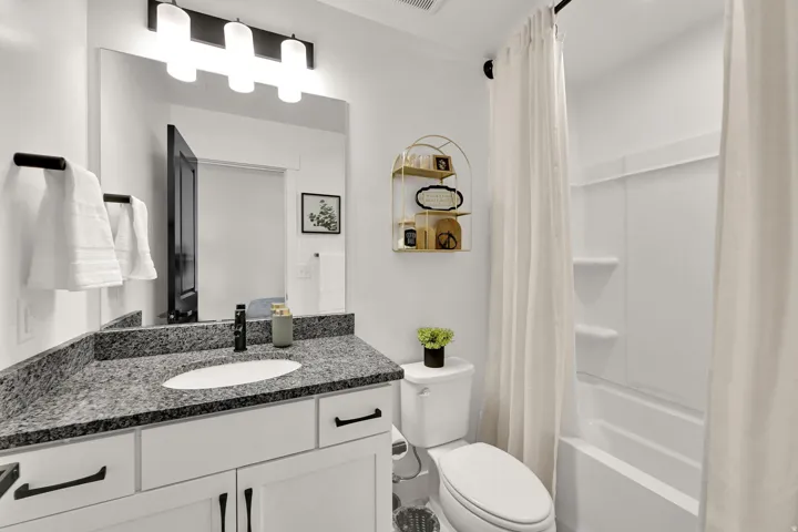 White vanity with dark hardware, speckled countertop, and under-mount sink