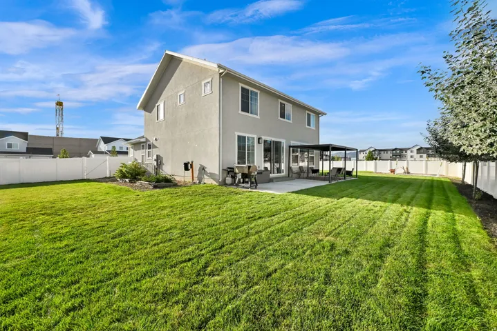 Expansive backyard featuring a manicured lawn, concrete patio with pergola, and white privacy fencing