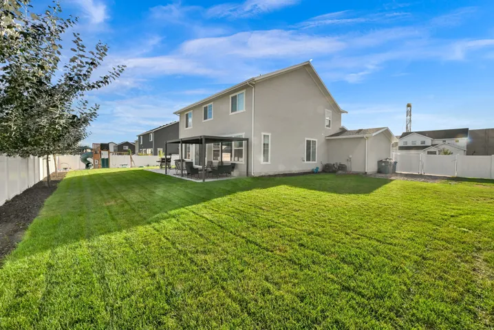 Expansive grassy yard with a covered patio area, stucco exterior, and white privacy fencing