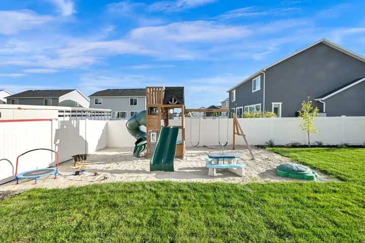 Expansive backyard with a manicured lawn, white privacy fencing, and a dedicated sand area