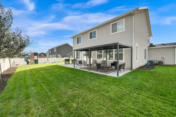 Expansive backyard featuring a manicured lawn, concrete patio with a permanent pergola structure, and a white privacy fence