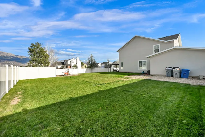Expansive backyard featuring a manicured lawn, a white privacy fence, and a gravel strip along the property structure