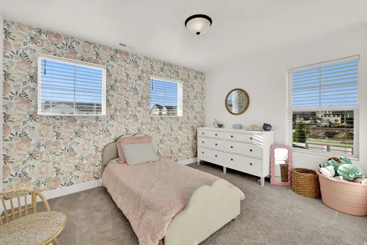 Wall-to-wall carpeting, three windows with blinds, floral accent wall, and a white dresser with multiple drawers