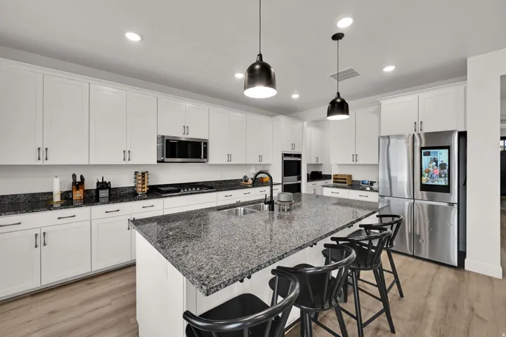 Gourmet kitchen featuring white cabinetry, granite countertops, stainless steel appliances, a large center island, and wood-finish flooring