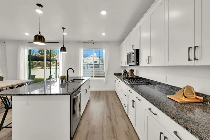 Contemporary kitchen featuring a large island, white shaker cabinetry, dark speckled countertops, and wood-finish flooring