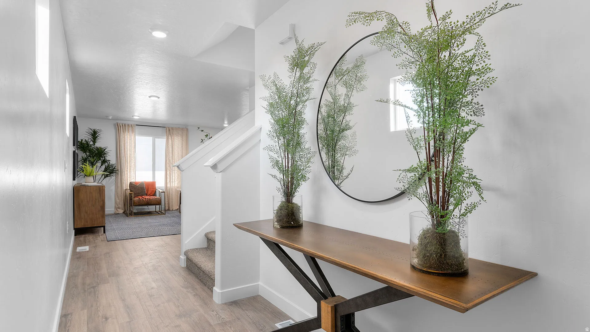 Wood-finish flooring, white painted walls, recessed lighting, carpeted staircase, and a wood console table