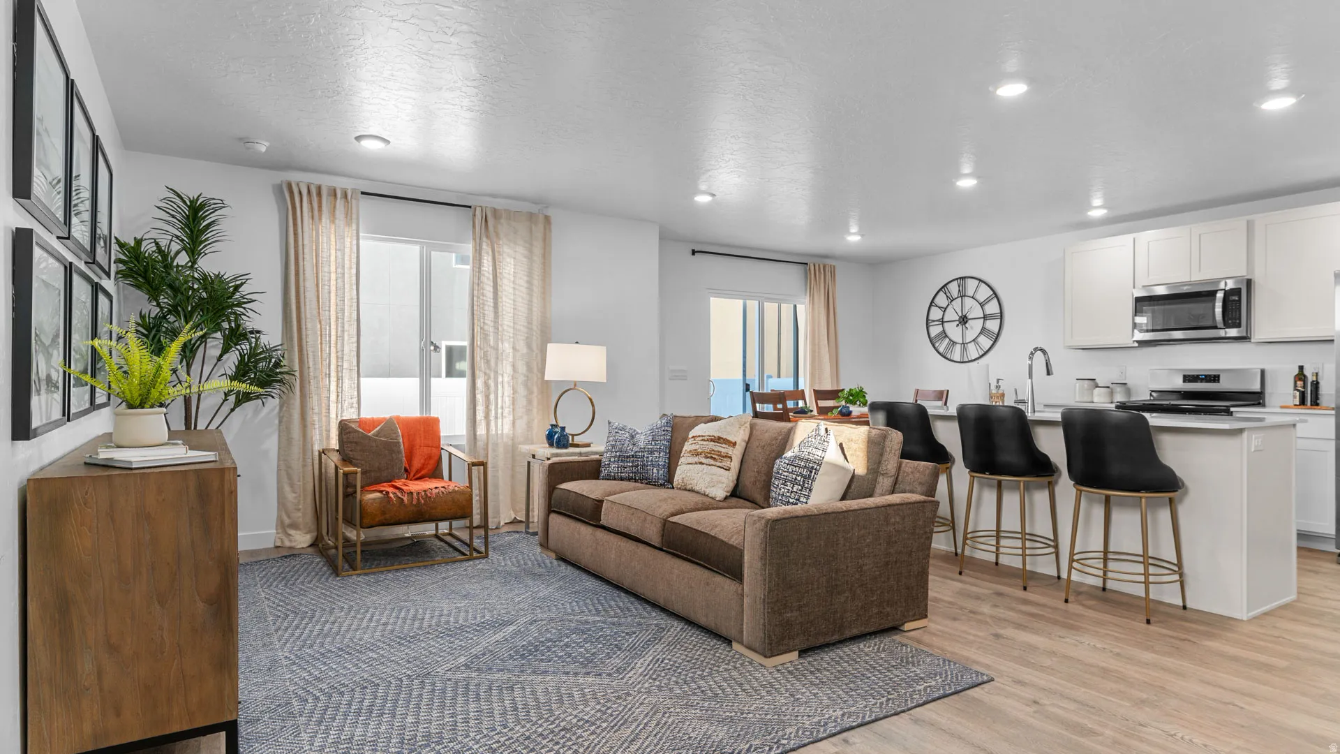 Open-concept living area with wood-finish flooring, recessed lighting, and a kitchen island featuring a sink and bar seating