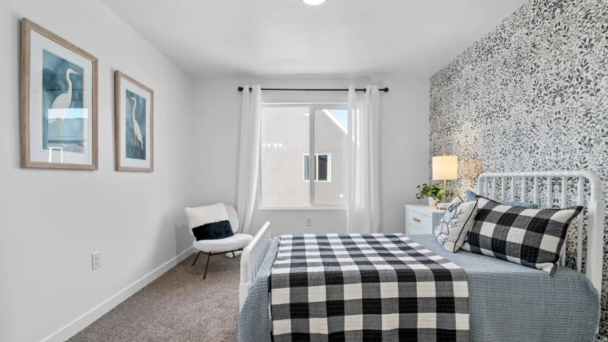 Carpeted flooring, window with white curtains, patterned accent wall, white painted walls, and a built-in light fixture