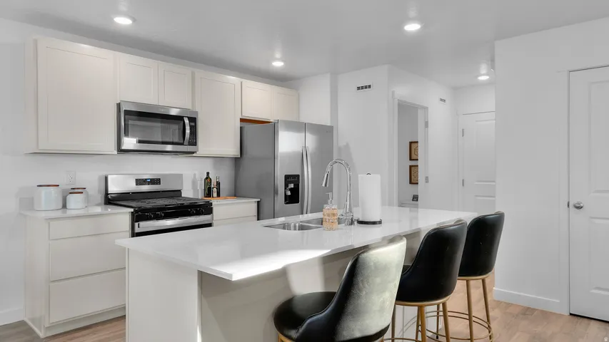 Kitchen featuring a stainless steel microwave, gas range, refrigerator, and a kitchen island with an integrated sink