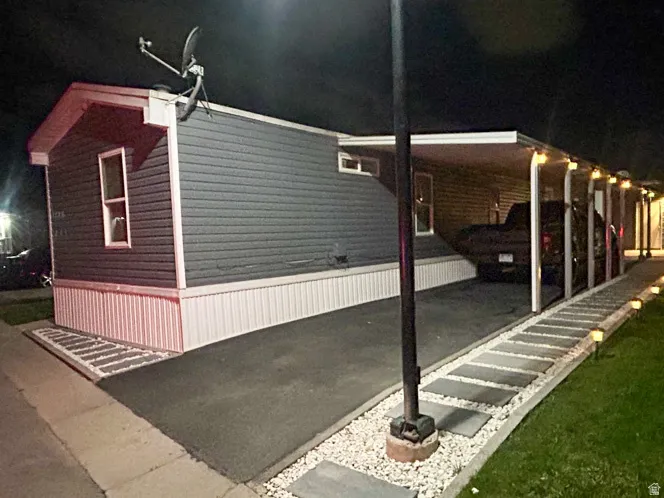 Night time picture of Carport with overhead lighting, asphalt driveway, decorative stone landscaping, and exterior wall siding