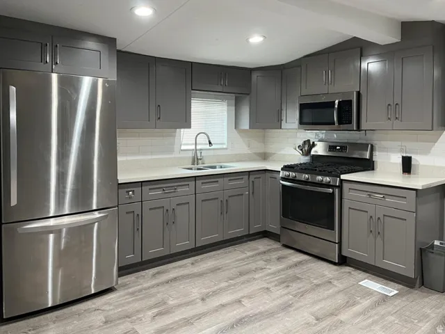 Modern kitchen featuring stainless steel appliances, grey shaker-style cabinetry, light-toned countertops, subway tile backsplash, and wood-finish flooring