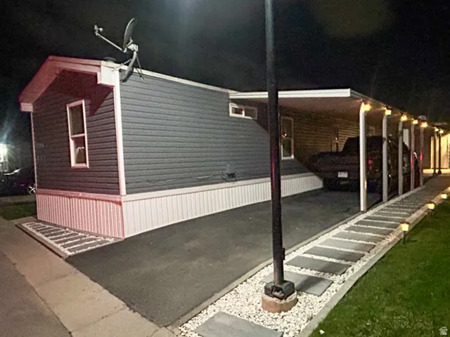 Night time picture of Carport with overhead lighting, asphalt driveway, decorative stone landscaping, and exterior wall siding