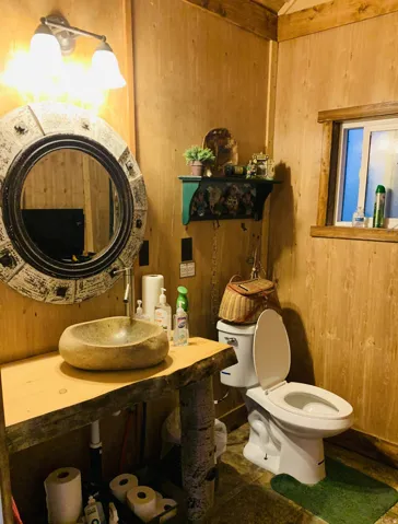 Wood-paneled walls and ceiling, stone vessel sink, custom wood vanity with live-edge top, double-light vanity fixture