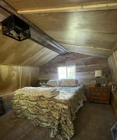 Vaulted ceiling with exposed beam, dual-pane window, wood-paneled wall, and carpeted flooring
