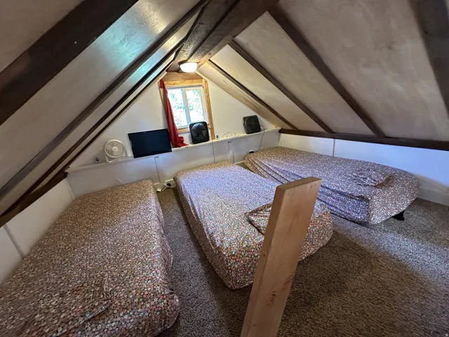 Loft space featuring sloped wood-paneled ceilings, exposed wood beams, a built-in window, and carpeted flooring