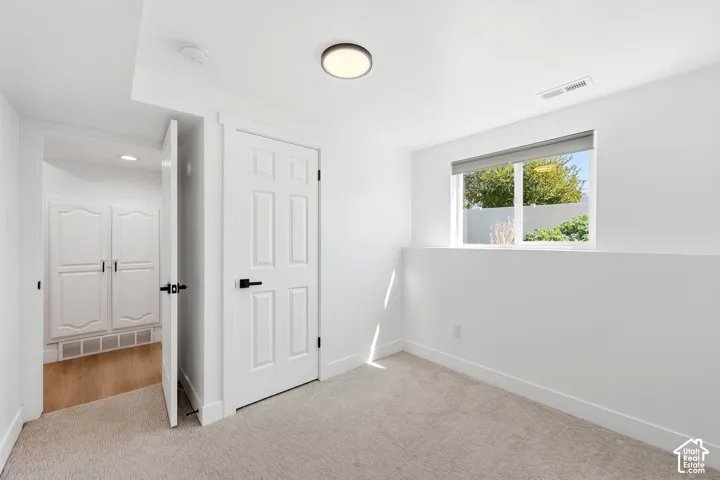 White interior walls, recessed window, light-toned carpet, paneled interior door with matte black hardware, and an overhead flush-mount light fixture