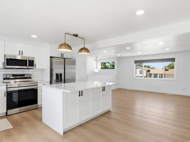 White kitchen cabinetry with black hardware, stainless steel appliances, a center island with a light-toned countertop, and wood-finish flooring