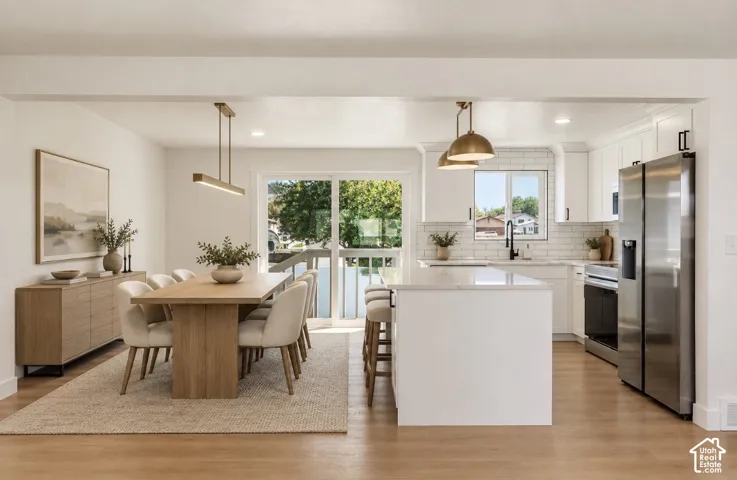 Open-concept kitchen and dining area featuring custom white cabinetry, stainless steel appliances, wood-finish flooring, and a large island with waterfall countertop